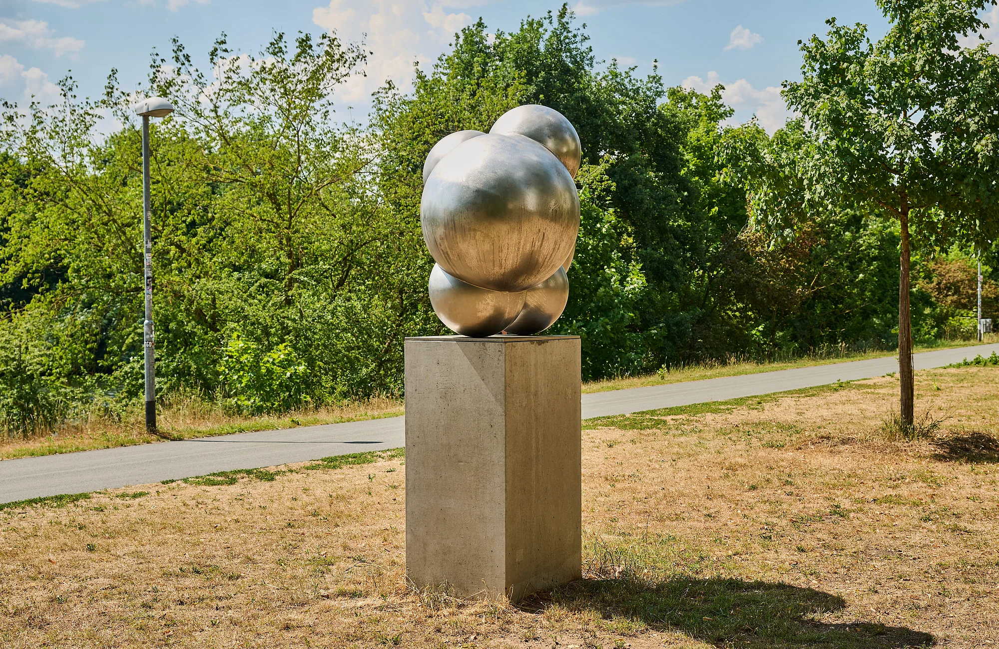 Die Skulptur H2O besteht aus Edelstahl und bildet zwei Wassermoleküle auf einem Steinsockel ab. Sie steht am Adenauerufer direkt am Regnitzradweg.