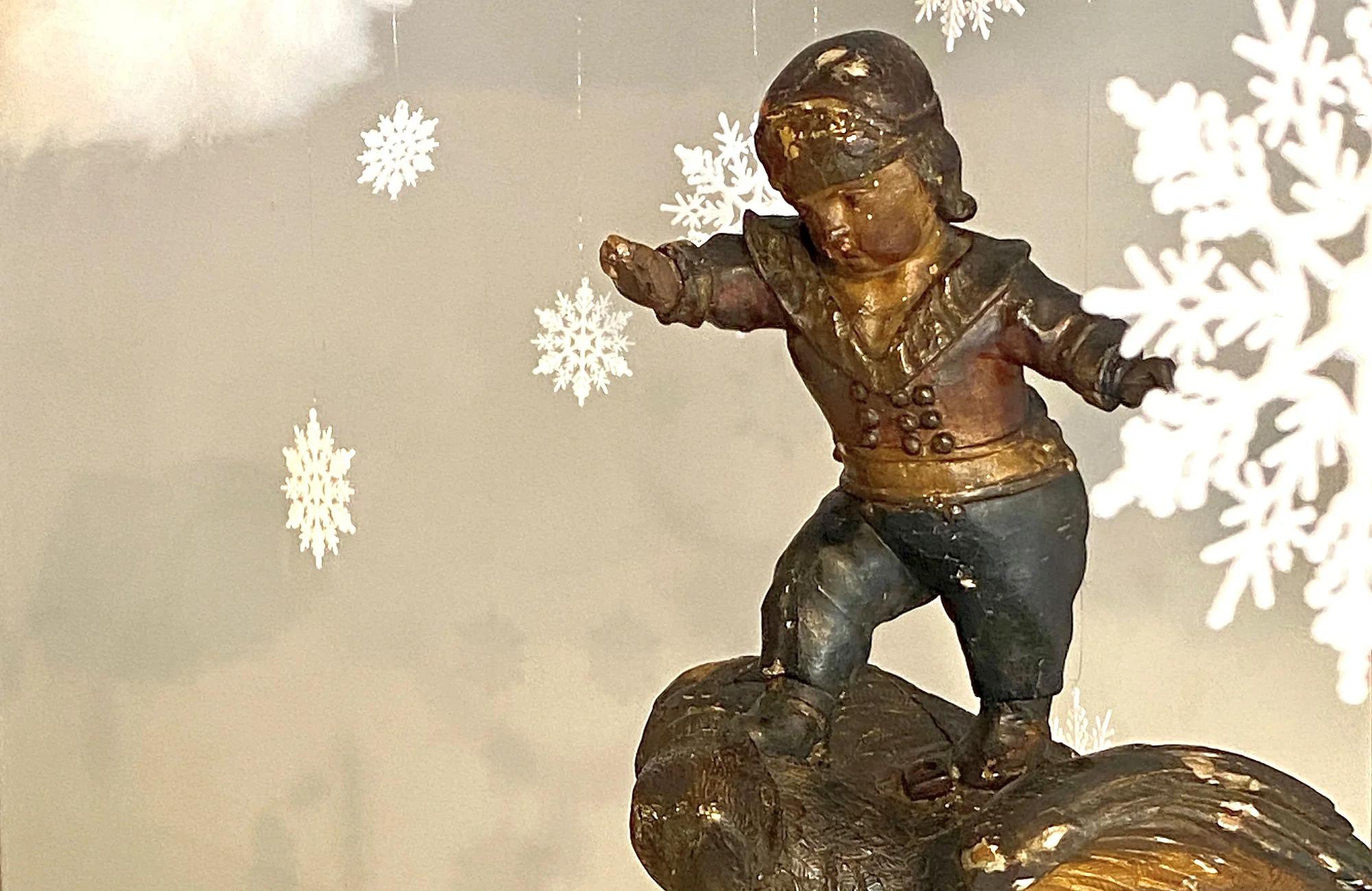 Ein Detail aus der Winterausstellung 2025/2026. Ein Putto auf einem Schlitten im Schnee.