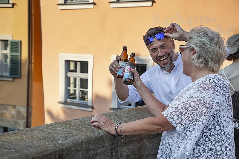 Zwei Personen stoßen mit Bierflaschen an vor der Rathausschänke.